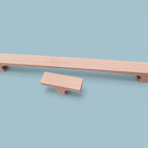 May include: Two wooden cabinet hardware pieces, a long handle and a smaller knob, are displayed against a light blue background. The wood has a natural, light brown color. The handle is rectangular with angled ends, and the knob has a similar design.