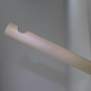 May include: A light-coloured wooden dowel with a curved notch at one end. The dowel is inserted into a white surface, suggesting a possible handle or support element. The wood grain is visible.
