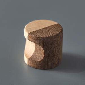 Puede incluir: Un pomo de madera con un diseño único, que presenta un patrón de veta de madera marrón claro y marrón oscuro. El pomo tiene una forma redondeada con un recorte en un lado, creando un asa.