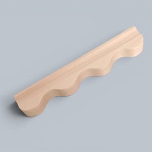 May include: A light-colored wooden shelf featuring a wavy, scalloped front edge. The piece is crafted from smooth, natural wood with visible grain patterns, showcasing a long, linear design with three distinct rounded curves along the front side.