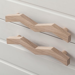 Può includere: Due maniglie per cassetti in legno con un design a zig-zag. Le maniglie sono di colore marrone chiaro e hanno una finitura in legno naturale.
