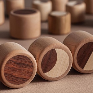 May include: Wooden decorative objects with a cylindrical shape. The objects are made of light-colored wood with dark wood accents on the ends. Some have a full circle of dark wood, while others have a crescent or diagonal design.