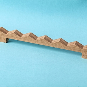 May include: A wooden handle with a unique stepped design. The handle is made of light brown wood and has a smooth finish.