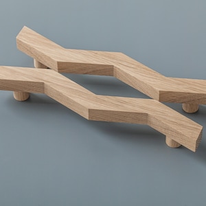 Op de afbeelding: Twee houten kastgrepen met een zigzagontwerp. De grepen zijn gemaakt van lichtbruin hout en hebben een natuurlijke afwerking.