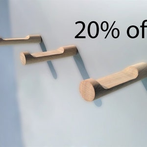 May include: Three wooden wall hooks with a natural finish are mounted on a light blue wall. Each hook has a cylindrical base and a curved top for hanging items. The text "20% off" is displayed in black.