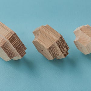 May include: Three light brown wooden geometric shapes are displayed against a light blue backdrop. Each shape features a distinct design with angled and curved edges. The visible wood grain provides texture to the objects, enhancing their appearance.