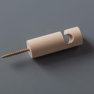 Può includere: Un gancio da parete in legno con una vite in ottone. Il gancio è cilindrico con un ritaglio curvo per appendere oggetti. La vite è lunga circa 5 cm. Il gancio è realizzato in legno chiaro.