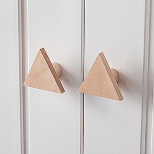Può includere: Due pomelli per armadio triangolari in legno di colore chiaro montati su una porta di armadio bianca.
