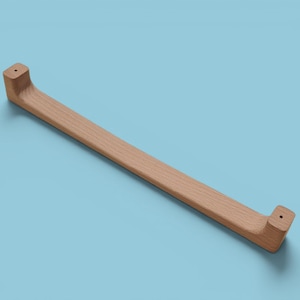 Puede incluir: Un tirador de armario de madera clara con una barra rectangular y extremos curvos. El tirador está hecho de madera natural y tiene un acabado liso. El tirador mide aproximadamente 30 cm de largo.