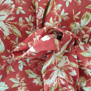 Könnte beinhalten: Roter Stoff mit Blumenmuster. Der Stoff zeigt weiße und hellbraune Blumen mit grünen Blättern.