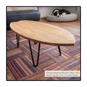 Pode incluir: Mesa de centro artesanal em forma de prancha de surf, com acabamento em carvalho claro. A mesa apresenta pernas de hairpin pretas e um design moderno de meados do século. O tapete é colorido e estampado.