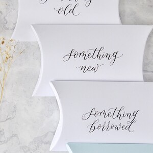 May include: Four white pillow boxes with the text "something old", "something new", "something borrowed", and "something blue" written in black calligraphy.