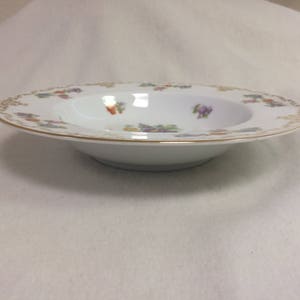 May include: White porcelain soup bowl with a gold rim and floral pattern. The bowl has a wide rim with a delicate design of colorful flowers and foliage. The interior of the bowl is plain white.