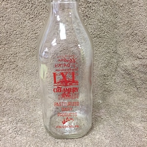 May include: Clear glass milk bottle with red lettering. The bottle has a wide base and a narrow neck. The text on the bottle reads "IXL Creamery, Pasteurized Dairy Products, Friedens, PA."