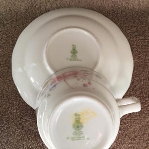 May include: White teacup and saucer set with a floral design in pink and blue. The teacup has a handle and sits on a matching saucer. The set is made of fine china.