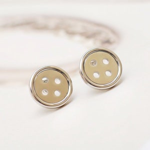 May include: A pair of silver button earrings with four holes in each button.