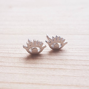 Può includere: Un paio di orecchini a bottone in argento a forma di occhio. Gli orecchini sono piccoli e delicati, con un design semplice.