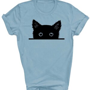 May include: A light blue t-shirt with a black silhouette of a cat peeking over the top. The cat has large blue eyes.
