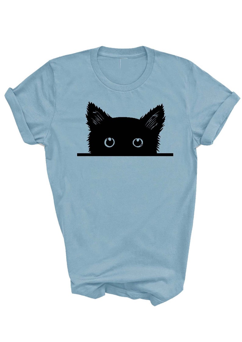 May include: A light blue t-shirt with a black silhouette of a cat peeking over the top. The cat has large blue eyes.