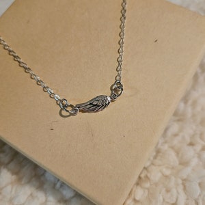 May include: A silver chain necklace with a small silver wing pendant.