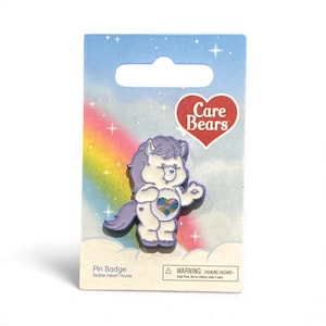 May include: A pin badge featuring Noble Heart Horse from Care Bears. The pin is white with purple accents, a rainbow heart, and a rainbow on the background. The Care Bears logo is in a red heart shape. The packaging has a warning about choking hazards.