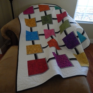 May include: A white quilt with a black and gray geometric design. The quilt features squares of various colors, including red, orange, yellow, green, blue, purple, and pink.