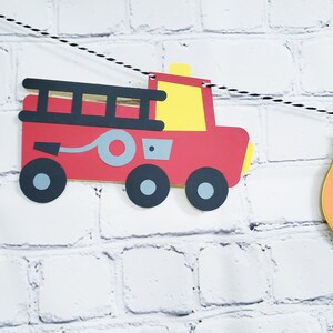 May include: Red fire truck paper cut-out with black wheels, a gray hose, and a yellow ladder. The fire truck is part of a paper banner with a yellow and orange flame cut-out.