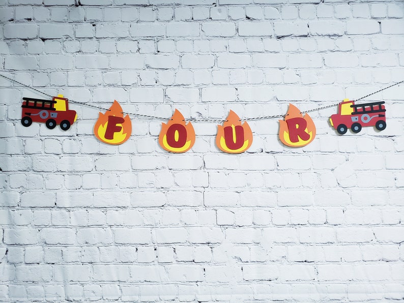 May include: Fire truck themed banner with red letters spelling out "FOUR" in a flame design. The banner is strung with red and white string and has a fire truck on each end.
