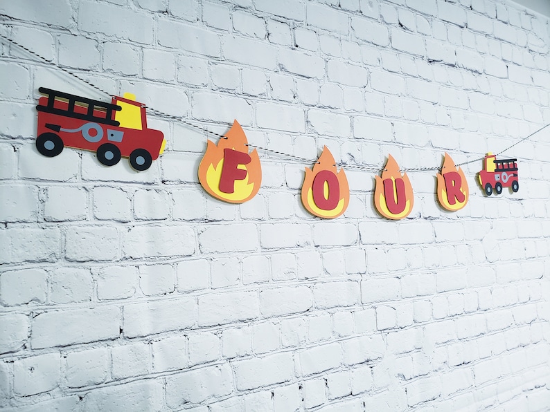 May include: Fire truck and flame-shaped letters spelling out "FOUR" on a white brick wall. This is a birthday banner for a child's fourth birthday party.