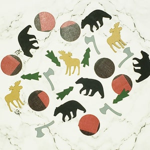 May include: A collection of woodland-themed paper cutouts on a white marble background. The cutouts include bears, moose, pine trees, and axes. The cutouts are in shades of black, brown, green, and yellow.