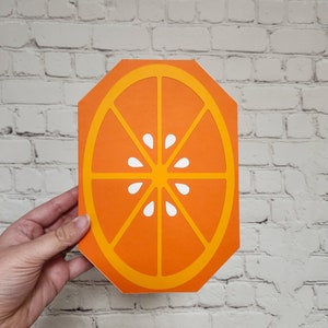 May include: Orange slice cutout with a yellow outline and white segments. The orange slice is a flat, decorative piece.