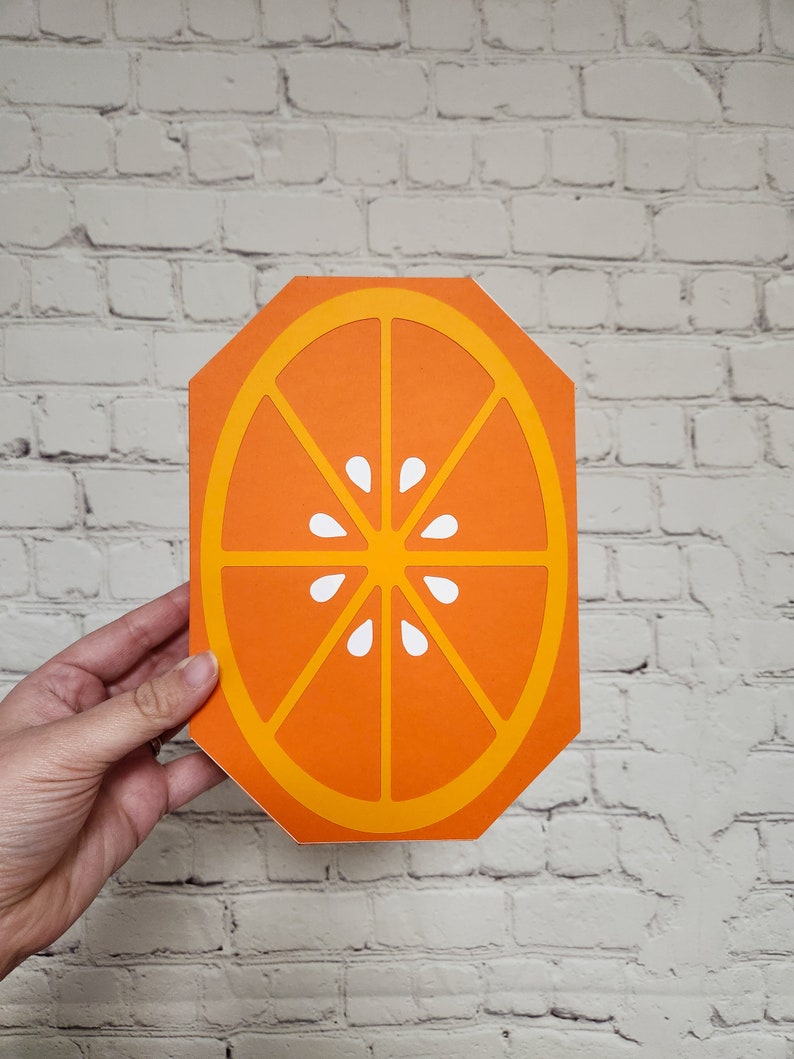 May include: Orange slice cutout with a yellow outline and white segments. The orange slice is a flat, decorative piece.