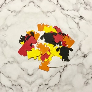 May include: A pile of red, yellow, orange, black, and white paper cutouts of fire trucks, flames, and dogs. The cutouts are on a white marble surface.
