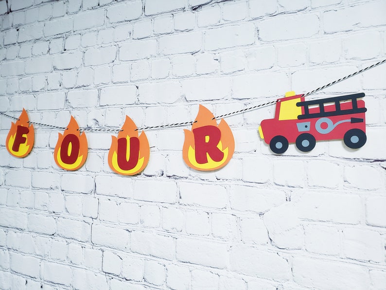 May include: Fire truck themed birthday banner with the word "FOUR" in red letters on orange flames. The banner also includes a red fire truck with black details.