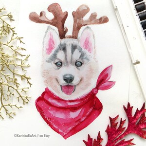 May include: Watercolor painting of a husky puppy wearing a red bandana and reindeer antlers. The puppy has a happy expression and is looking directly at the viewer. The painting is on a white background.