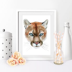 May include: Watercolor painting of a cougar's face with blue eyes. The cougar is looking directly at the viewer. The background is white.