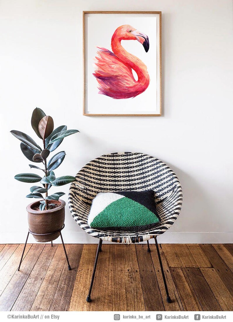 May include: A framed watercolor painting of a pink flamingo with a white background. The painting is hanging on a white wall above a black and white striped wicker chair with a green and white pillow.