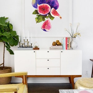 May include: A framed watercolor painting of a bunch of purple figs with green leaves. The painting is hanging on a white wall above a white dresser with a yellow chair in front of it.