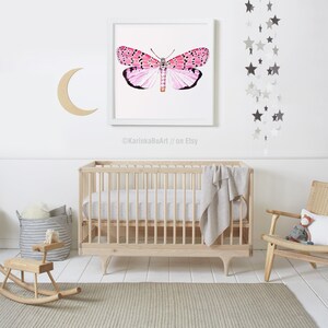 May include: A white crib with a white and gray patterned sheet and a gray blanket. A wooden rocking horse and a basket with a gray and white patterned blanket are in the foreground. A framed print of a pink butterfly is on the wall above the crib. A silver star mobile hangs from the ceiling.