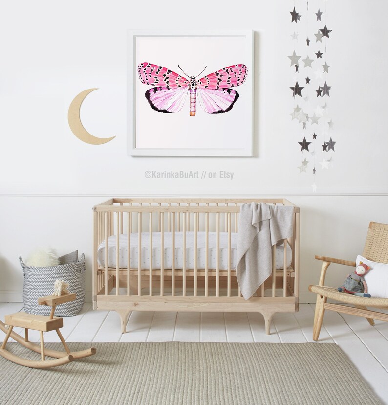 May include: A white crib with a white and gray patterned sheet and a gray blanket. A wooden rocking horse and a basket with a gray and white patterned blanket are in the foreground. A framed print of a pink butterfly is on the wall above the crib. A silver star mobile hangs from the ceiling.