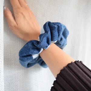May include: A blue and white denim scrunchie hair tie. The scrunchie is made of soft, stretchy fabric and is perfect for holding back hair.
