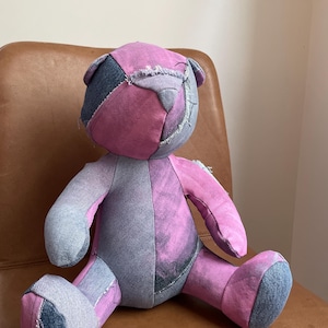 Könnte beinhalten: Ein Patchwork-Teddybär aus Jeans und rosa Stoff. Der Bär sitzt auf einem braunen Ledersessel.
