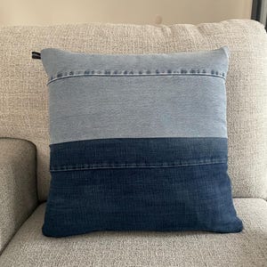 Könnte beinhalten: Ein blaues Jeans-Kissen mit einem hellblauen Streifen und einem dunkelblauen Streifen. Das Kissen liegt auf einem hellgrauen Sofa.
