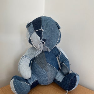 Könnte beinhalten: Ein Teddybär aus Patchwork-Jeans mit einem blauen, weißen und schwarzen Farbmuster. Der Bär sitzt auf einer Holzoberfläche.