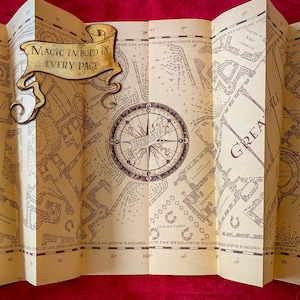 May include: A folded parchment map featuring intricate dark brown ink illustrations of castle grounds, a central compass rose, and the text "MAGIC IMBUED IN EVERY PAGE" on a decorative scroll. The map includes labels like "GREAT HALL" and "COURTYARD".