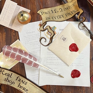 May include: A collection of printed stationery including a Hogwarts acceptance letter with a red wax seal, a uniform list, and a small card. A white and maroon feather quill, a metal wand, a brass inkwell, and several loose red wax seals are arranged on the paper.
