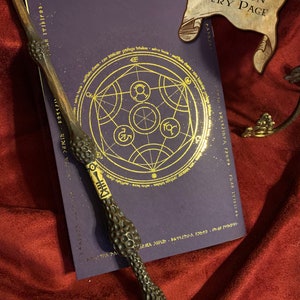 Purple book with intricate gold astral design on red velvet. A detailed wand lies beside it. Top banner reads 'Magic on Every Page'. Enchanting accessory for those passionate about the mystical arts.