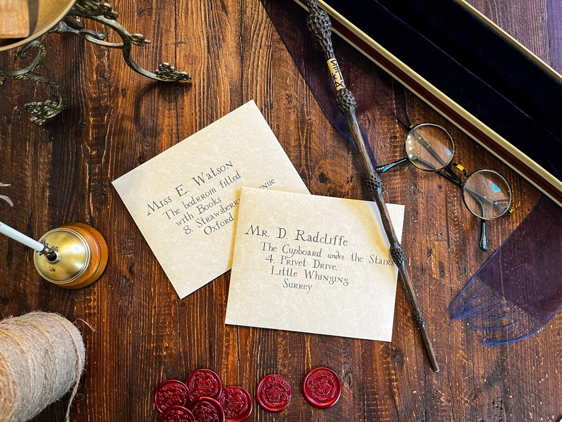 Vintage themed stationary custom parchment letters addressed to fictional characters, an intricately designed wand, round glasses, red wax seals, and an old fashioned bell on a rustic wooden table, accompanied by a twine spool and book edge.