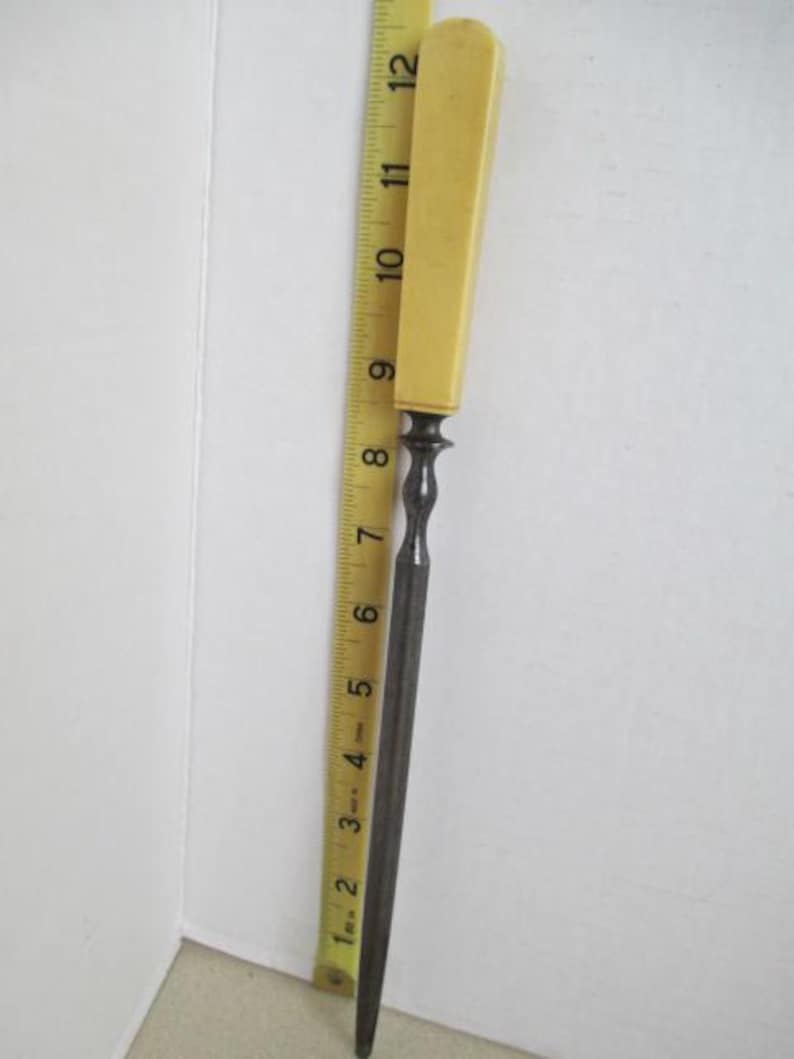 Pu&ograve; includere: Una lima di metallo vintage con un manico in osso. La lima &egrave; lunga circa 25 cm e ha una punta arrotondata. Il manico &egrave; di colore giallo pallido.
