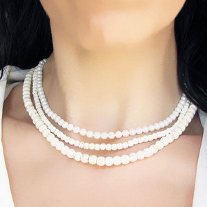 Puede incluir: Un collar de perlas de tres hileras con perlas blancas. El collar lo lleva una persona con el pelo largo y negro.